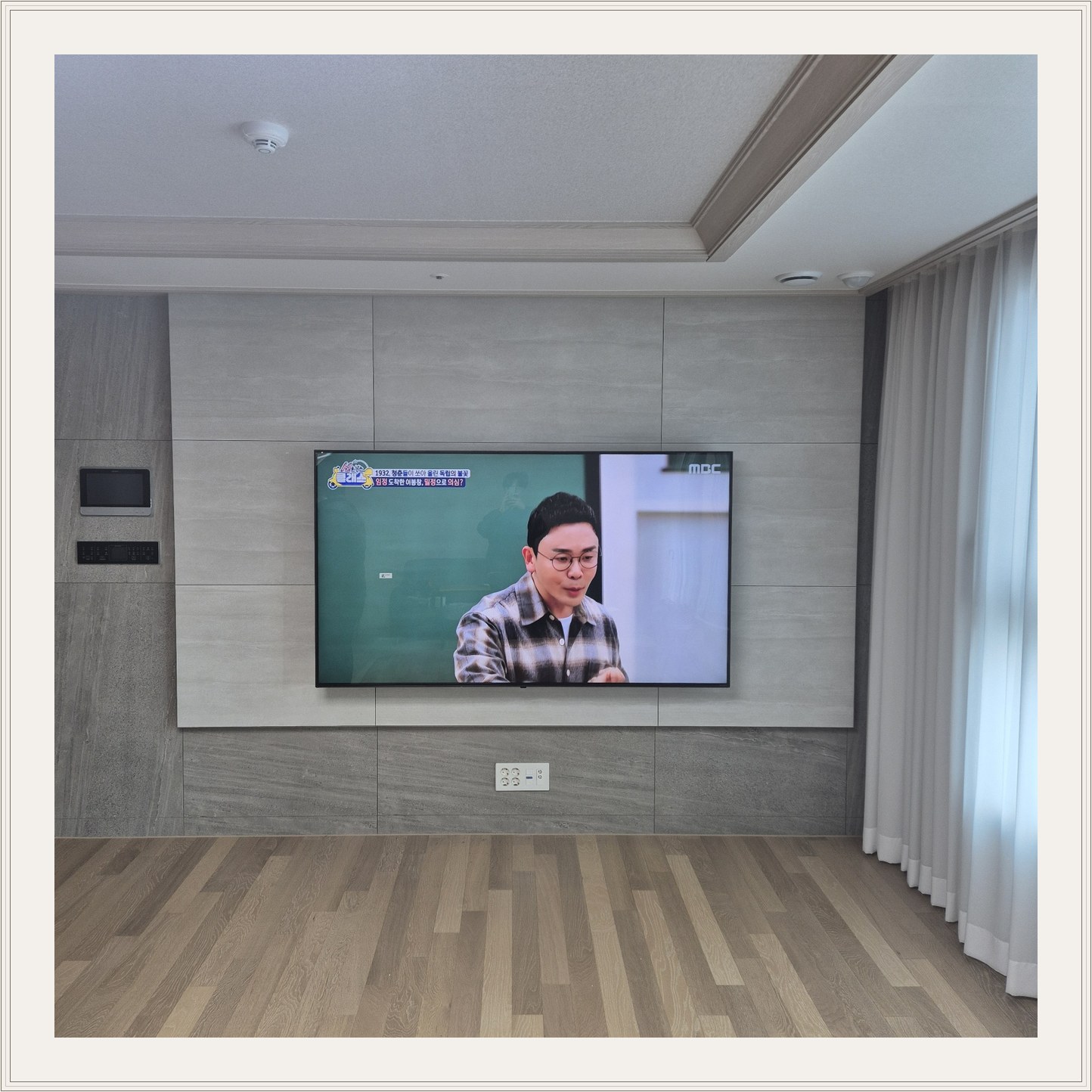 거실 회색 패널과 벽걸이 TV, TV 아래 콘센트와 양쪽 마감 판넬의 대비가 뚜렷합니다