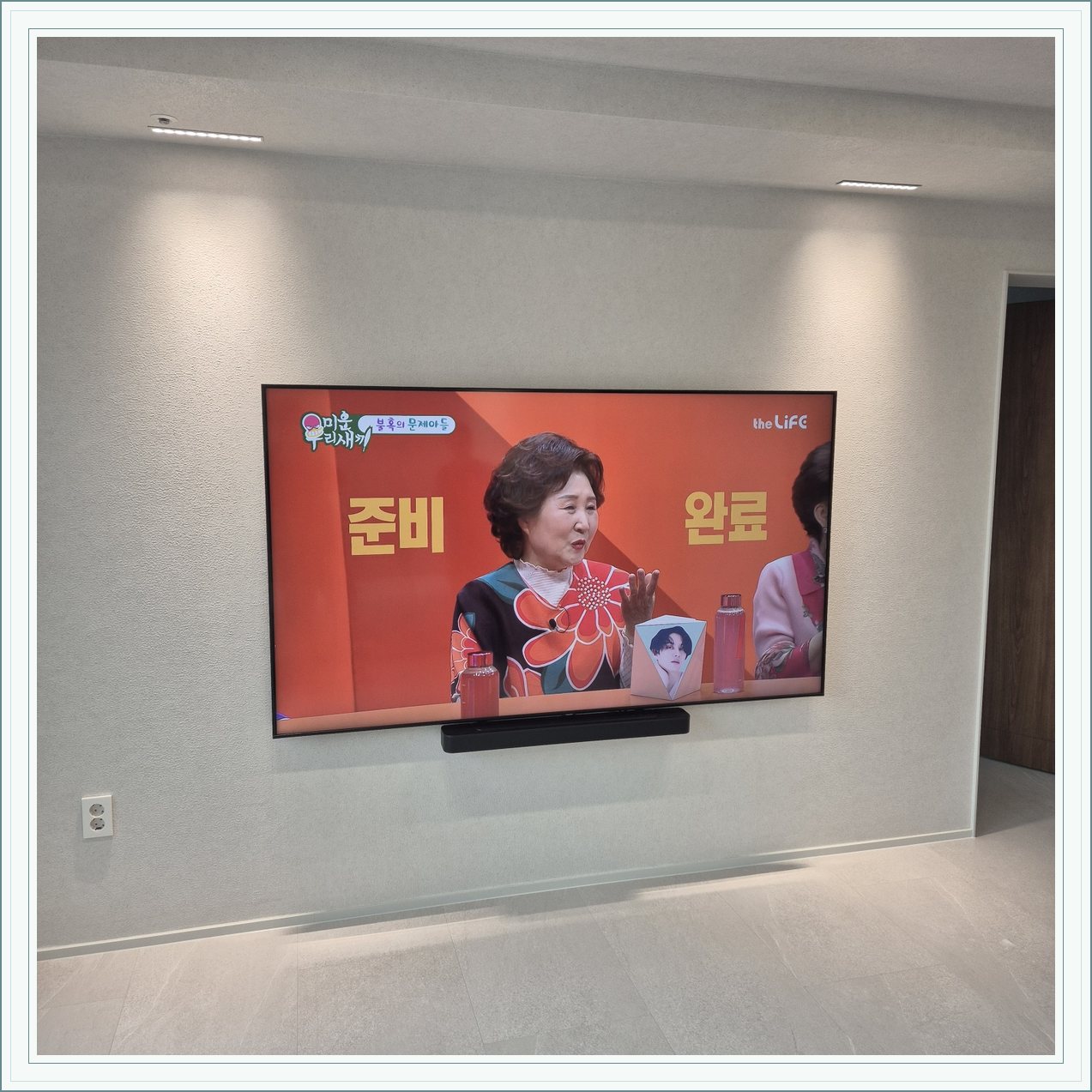 조명이 비추는 미색 벽과 사운드바, 사운드바와 벽면의 간격이 한눈에 들어옵니다