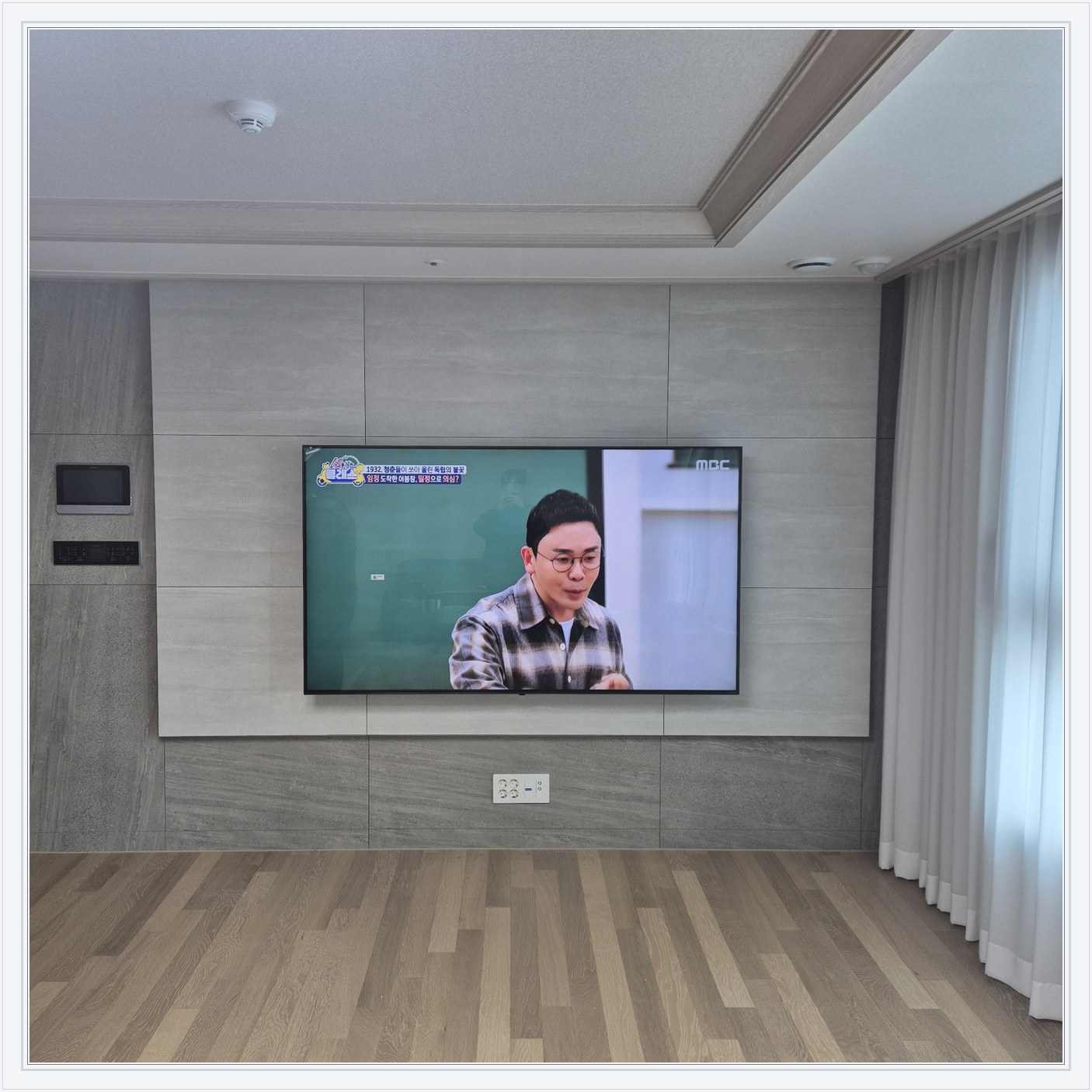 거실 회색 패널과 벽걸이 TV, TV 아래 콘센트와 양쪽 마감 판넬의 대비가 뚜렷합니다