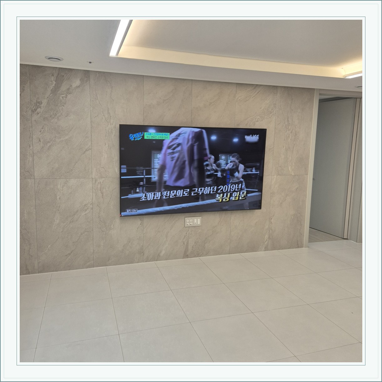 석재 느낌 벽면을 정면에서 본 TV, 벽 마감의 세로 이음선이 TV 양옆에 남아 있습니다