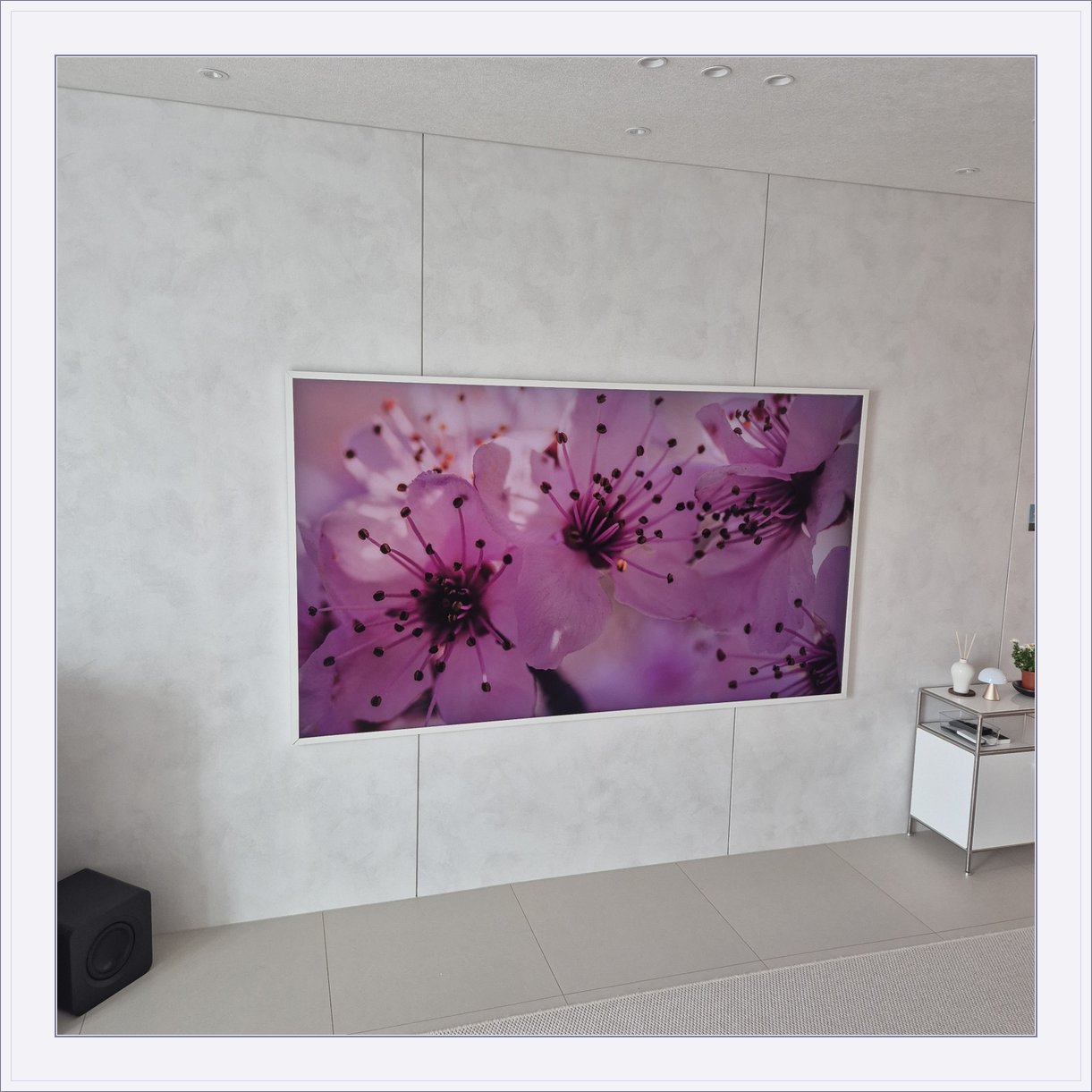 꽃 화면이 나오는 흰색 프레임 TV, 밝은 패널 위 흰 테두리와 꽃 영상의 색 대비가 큽니다