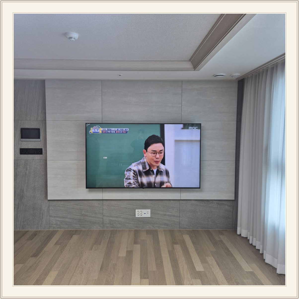 거실 회색 패널과 벽걸이 TV, TV 아래 콘센트와 양쪽 마감 판넬의 대비가 뚜렷합니다
