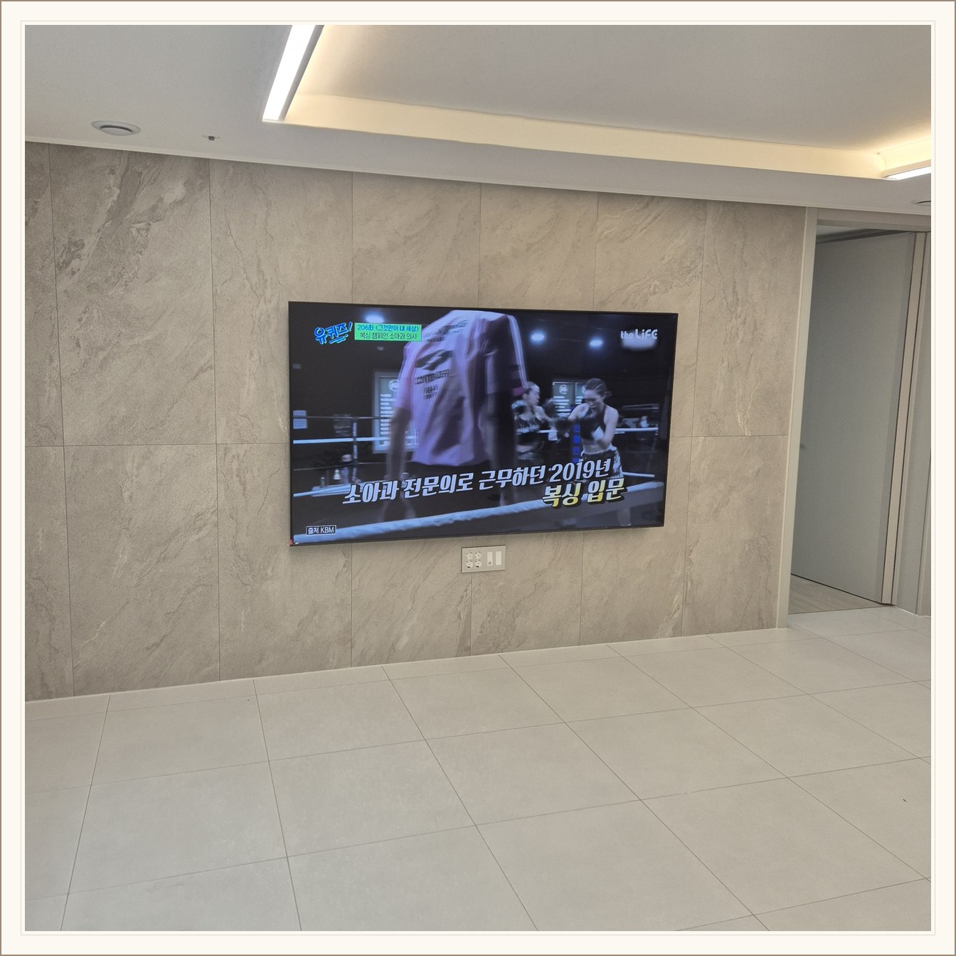 석재 느낌 벽면을 정면에서 본 TV, 넓은 바닥 여유와 조명 라인이 동시에 보입니다